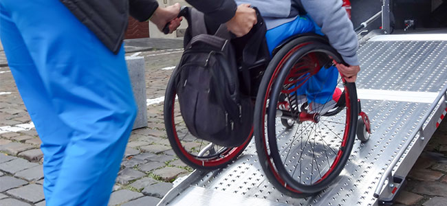 A patient in a wheelchair being helped from an ambulance.